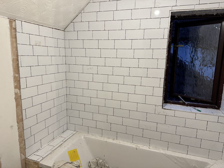 A bathroom tiled in white metro tiles around a bath and a window opening