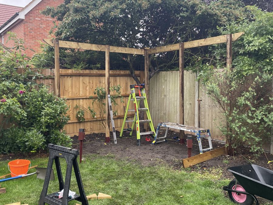 Pergola posts and head timbers standing in a garden with a trestle, ladder and wheelbarrow alongside