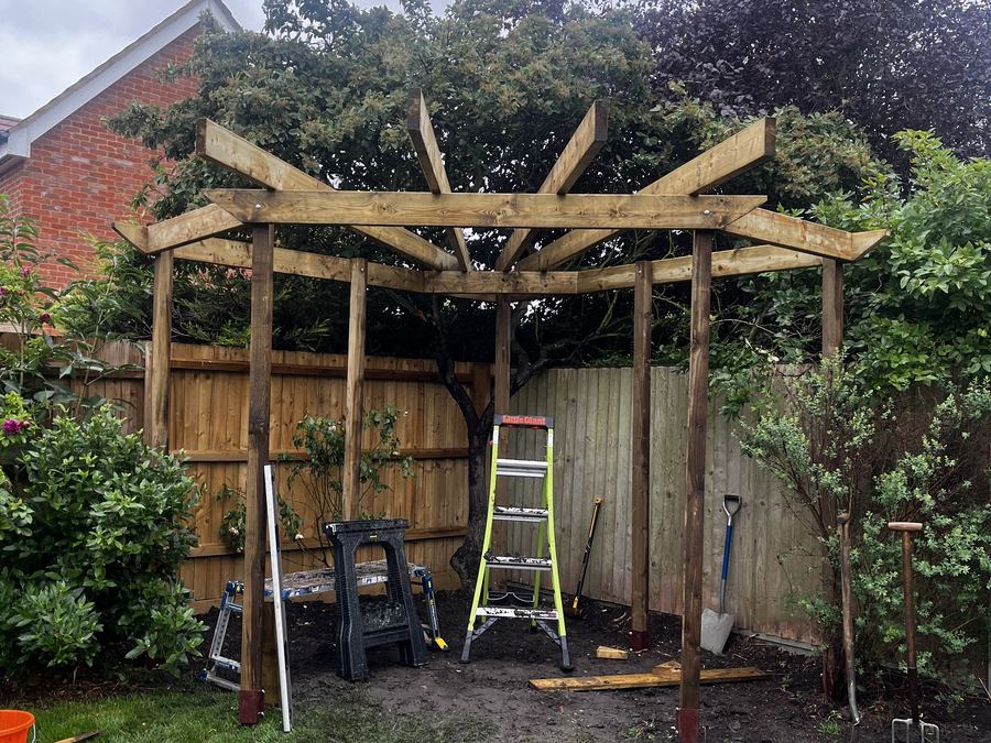 The completed timber frame of a garden pergola with a stepladder and tools alongside